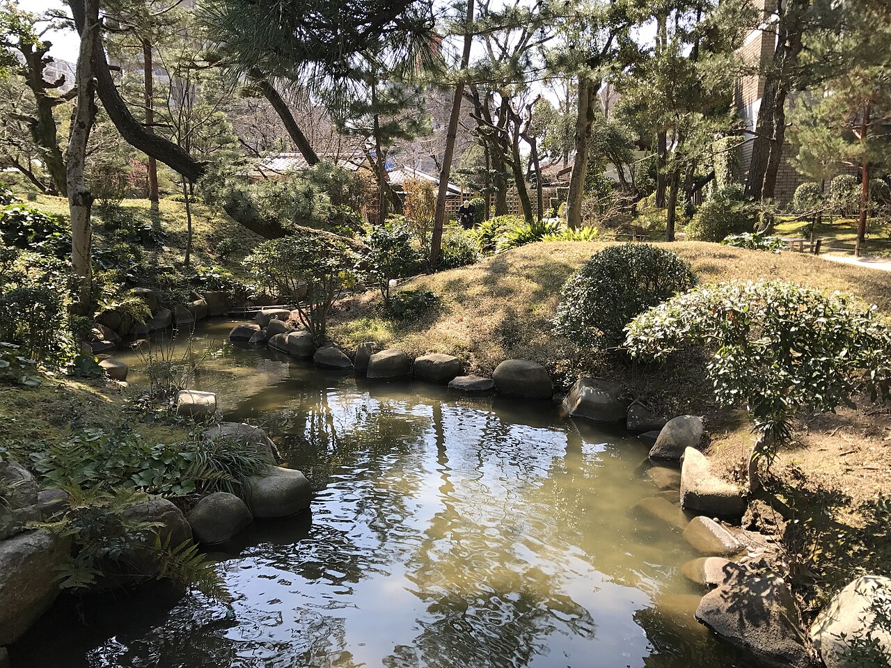 縮景園の石蟾橋から望む流れ。池のような水面の周りに松や草木が茂る