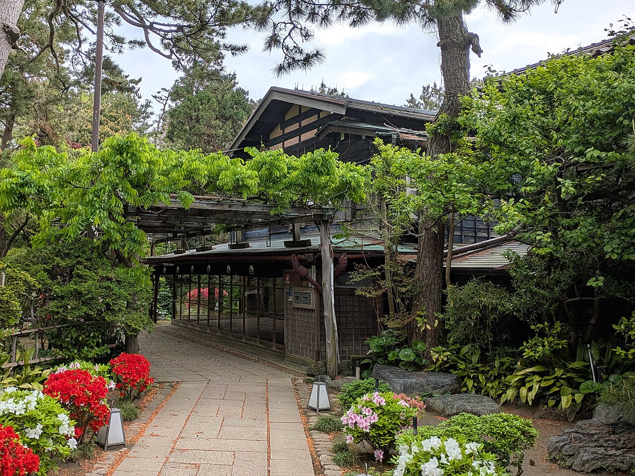 松と藤棚、石畳の通路のある行形亭の主屋