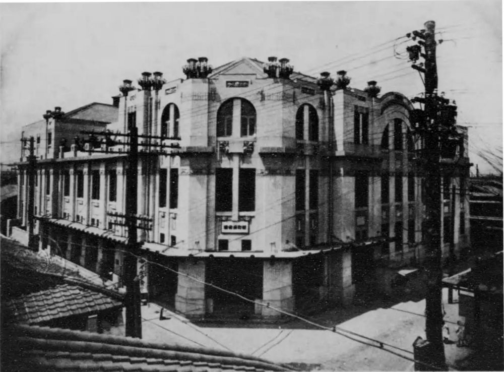 電柱と電線に囲まれて建つ、アーチ窓を並べた洋風の新町演舞場の白黒写真