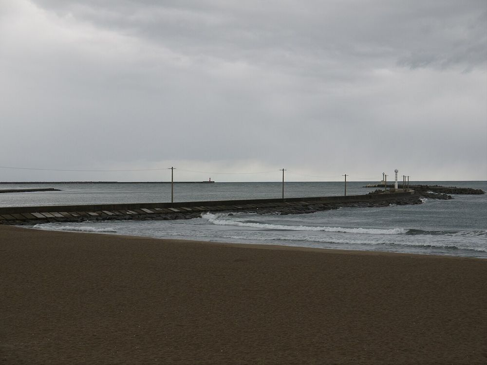 海に向かって細長く延びる三国湊の堰堤。曇り空の下の砂浜から撮影